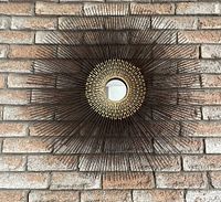 Front view of sunburst metal frame mirror mounted on brick wall
