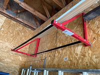 Side angled view of wall-mounted tire rack showing red metal bracket and black metal bar attached to wood panel