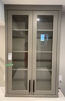 Front view of gray tall upper cabinet with two glass doors revealing three interior shelves.