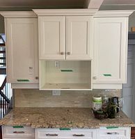 Overall view of three upper white kitchen cabinets installed above countertop with crown molding