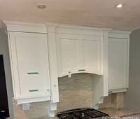 Installed view of two white upper cabinets flanking a decorative valance over a stove area