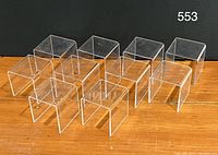 Photo showing 10 clear acrylic display riser units arranged in two rows, each unit roughly cube shaped and transparent, displaying minor surface scratches.