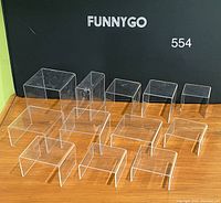 12 clear acrylic display risers of different sizes and shapes arranged on wooden surface with scratches on surfaces visible.