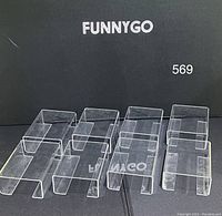 Top view of eight clear acrylic U-shaped display risers placed in two rows against a black background, brand FunnyGo visible.