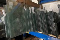 Multiple stacks of clear glass panels showing bevel edges, labeled with size notes, stored vertically on a rack.