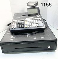 Photo of Casio SE-3000 cash register placed on top of a black metal cash drawer, showing keypad, displays, keys, and power cord.