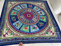 Full view of the large silk scarf laid flat, showing vibrant circular mandala floral design in blue, green, red, purple and cream.
