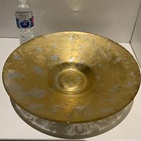 Front view of large glass decorative platter/bowl with gold and silver mottled finish, placed next to a water bottle for scale.
