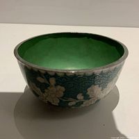 Front angle view of small green cloisonné bowl showing floral enamel decoration and silver-tone rim.