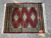 Full view of the small handwoven Persian rug on asphalt, showing its geometric diamond design and fringed edges.