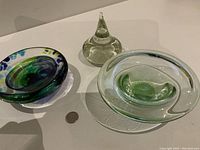 Three vintage mouth blown glass items on white surface: blue/green bowl with dots, clear glass bowl with green swirl, clear glass pointed art piece