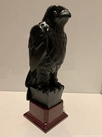 Front left angle view of vintage black bird statue on red base showing glossy surfaces and detailed feather texture.