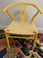Frontal view of the yellow ELTE wishbone chair showing the woven natural fiber seat and curved backrest on a colorful rug.