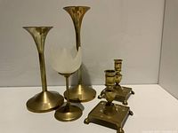 Four vintage brass candlesticks including pair of trumpet-shaped, frosted glass tulip-shaped, and square-based with ball feet candlesticks.