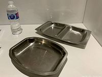 Photo showing two stainless steel serving trays: one single-compartment with handles and the other divided into three compartments, with a water bottle for scale.