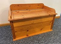Front view of the rectangular wooden bench with hinged lid closed, showing natural wood grain and knots.