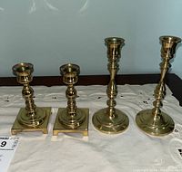 Four brass candle holders arranged in a row, showing two pairs of different heights and base shapes
