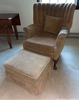 Side angle of beige cushioned armchair with rolled arms and matching ottoman on carpeted floor