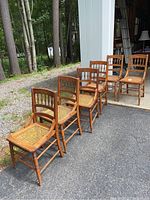 Six wooden cane side chairs arranged in two rows outside on driveway with garage in background