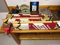 Wooden double bar clamps in red and white Shopsmith packaging stacked on bench with incidental items