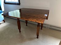 Front view of wooden dropleaf table with two extended leaves, showing wood grain surface and turned legs.
