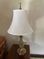 Full view of the solid brass Stiffel table lamp with white bell-shaped fabric lampshade on a wooden table.