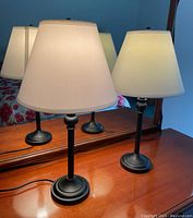 Pair of two matching table lamps in black metal bases and white fabric shades with visible marks, photographed on wooden furniture in front of a mirror.