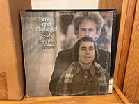 Simon and Garfunkel Bridge Over Troubled Water album cover showing wear and fading on a wood shelf