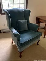 Front view of blue Hallagan upholstered wing back chair with matching throw pillow.
