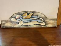 Front view of the hand-painted winter wooden wall plaque resting on a wood surface, showing the flying snowman with blue scarf and golden wings
