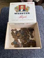 Overhead image of the vintage Webster Royals cigar box opened, showing a large quantity of unsorted wheat pennies inside.