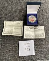 1999 American Eagle Silver Dollar coin displayed in blue velvet-lined box, with paperwork including Certificate of Authenticity and informational card.