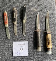 Set of five cutting tools displayed on a gray carpet, including three folding knives and two fixed blade knives with leather-wrapped handles.