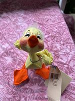 Front view of the 5-inch yellow duck figurine showing felt material, orange feet and beak, hand-painted facial details, and original tag attached.