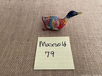Photo of colorful antique tin duck toy from front angle showing painted feather details and yellow beak with key.