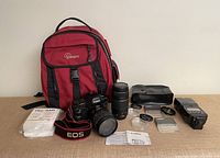 Overview of lot showing Lowepro backpack, Canon 5D with lens, second lens, flash, diffusers, filters, strap and manual