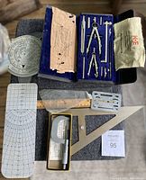 Various drafting and measuring tools laid out on a surface showing compass set, rulers, triangle, French curve, micrometer and others.