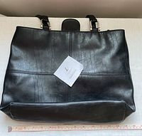 Front view of black Liz Claiborne faux leather purse showing smooth textured surface, handle hardware, and approximate width using a measuring ruler.