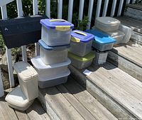 Photo of stacked plastic storage containers of varying sizes and lid colors on wooden steps outdoors.