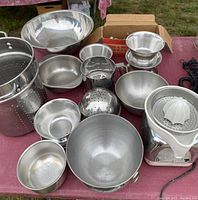Photo showing multiple stainless steel bowls and colander, vintage electric juicer with plastic juicing cone, and meat grinder box in background.