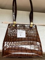 Front view of brown crocodile leather purse with a MaxSold number card on it showing scale and size.