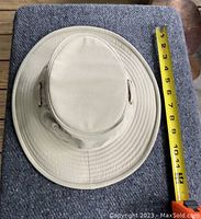Top-down photo of beige Tilley hat lying flat next to a tape measure showing around 11 inch diameter.