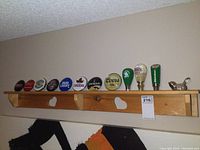 Wide shot of wooden shelf mounted on wall holding multiple beer tap handles and round glass beer tap signs.