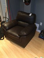 Full front-angle view of a brown faux leather armchair showing cushions and overall shape.
