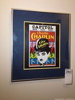 Framed Charlie Chaplin poster hanging on wall, showing full frame and mat with colorful graphic.