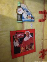Photo showing the Coca Cola plak board sign of Santa Claus holding a bottle and the plastic Coca Cola clock with polar bears