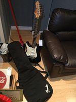 Full view of Barracuda electric guitar on stand next to Fender soft case.