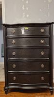 Front view of black high boy dresser showing five curved drawers with round metal pulls.