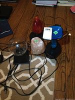 Three small table lamps on the floor showing cords. Includes red glass lamp, blue glass lamp, and pink salt lamp.