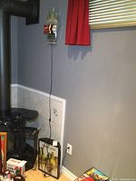 Shows Tuborg Beer light-up sign leaning against the wall near a wood stove, with attached power cord visible.